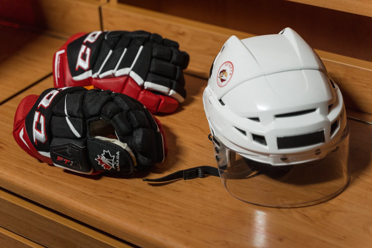 Close-up of hockey gear including helmet and gloves on a wooden bench.